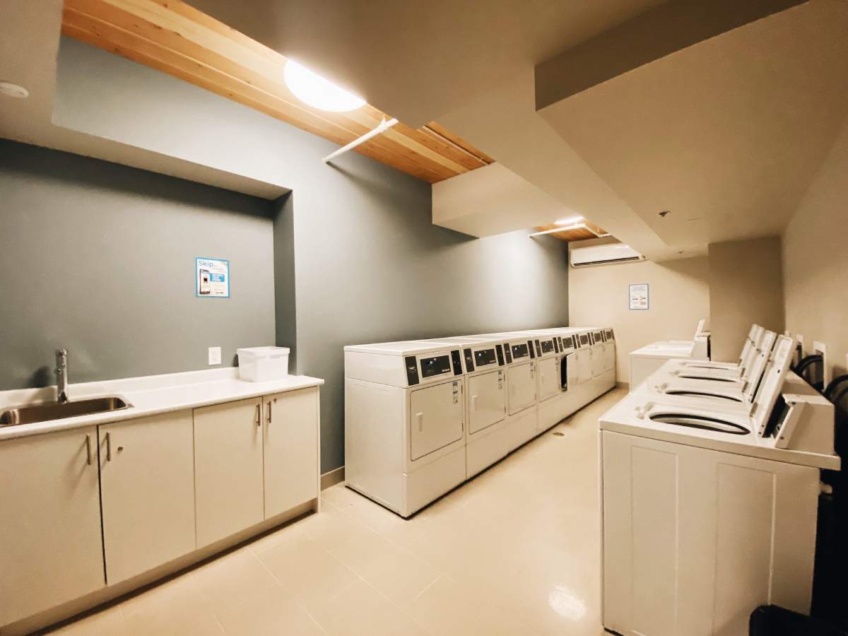 A clean and well-lit laundry room featuring multiple washing machines and dryers lined up along the walls.