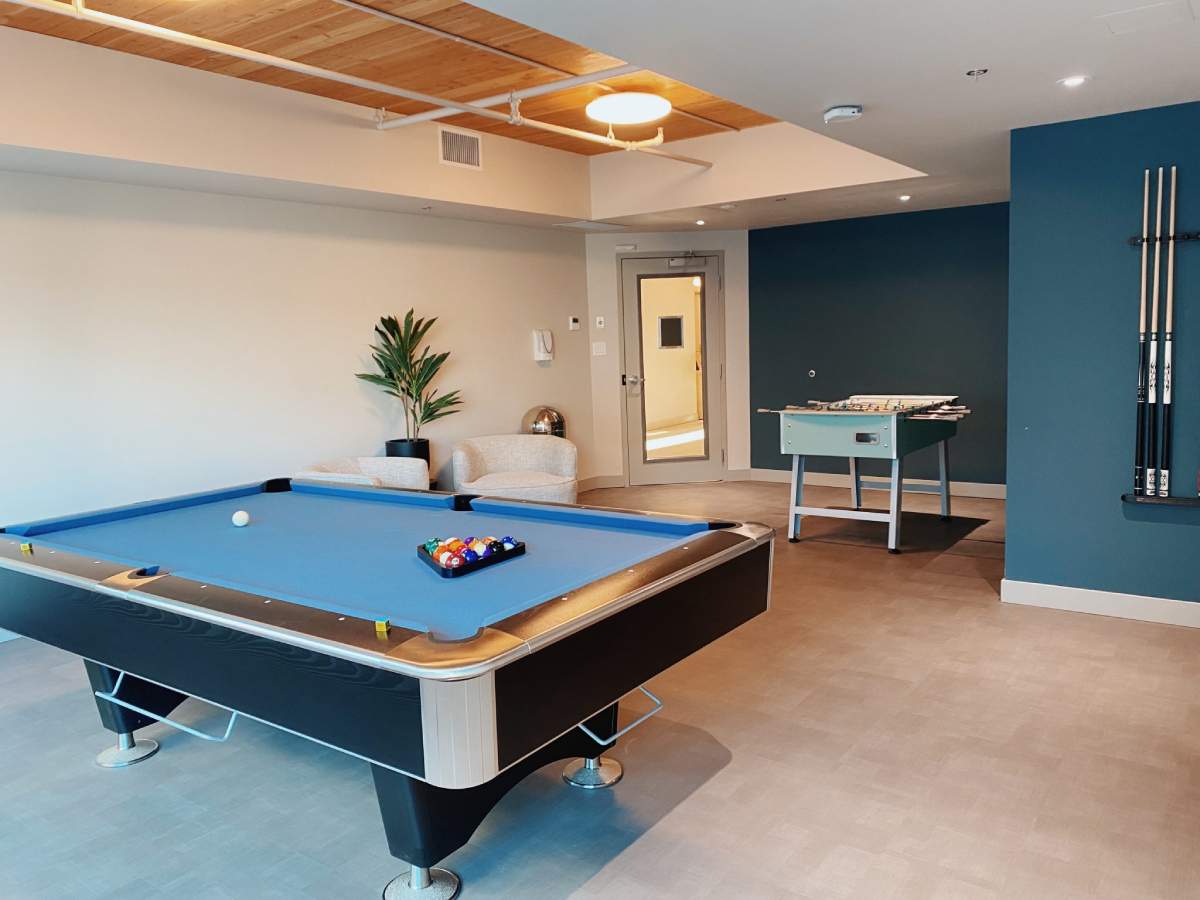 A recreational room featuring a modern pool table with a blue felt and a foosball table.